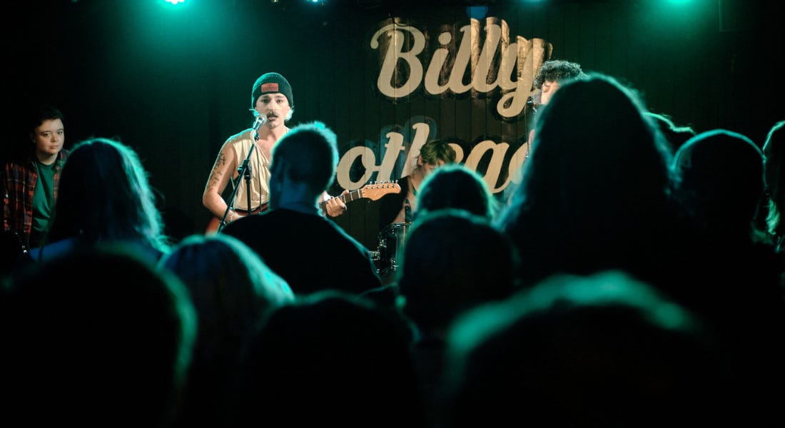 A crowd of people standing in front of a stage with a male singing A crowd of people standing in front of a stage with a male singing