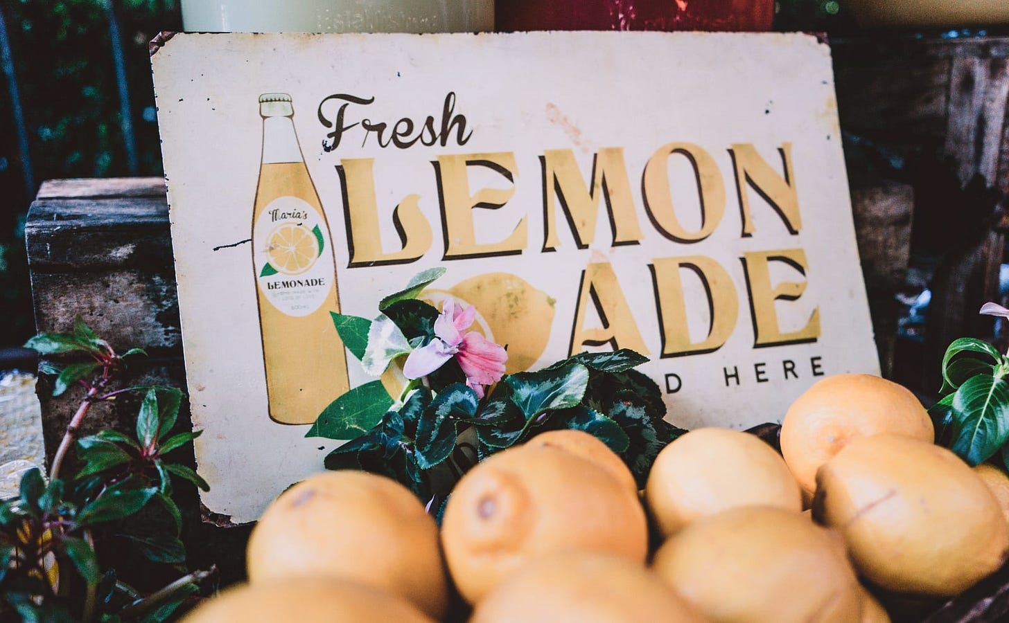 old-fashioned sign that says fresh lemonade with an illustration of a glass bottle of lemonade in the background with a pile of cheerful lemons in the foreground