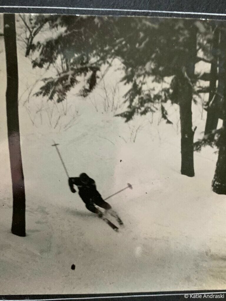A skier makes a sharp turn on a snowy slope surrounded by trees.