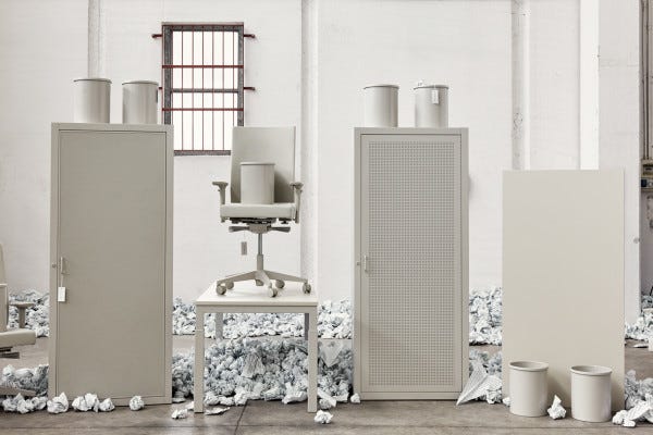 Photo from an art installation of white IKEA-style chairs, bins and closets surrounded by balls of paper, in a totally white room.