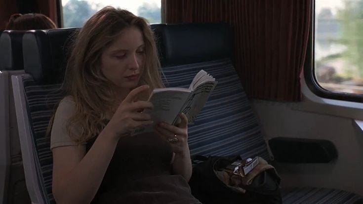 This may contain: a woman reading a book while sitting on a train seat in front of a window