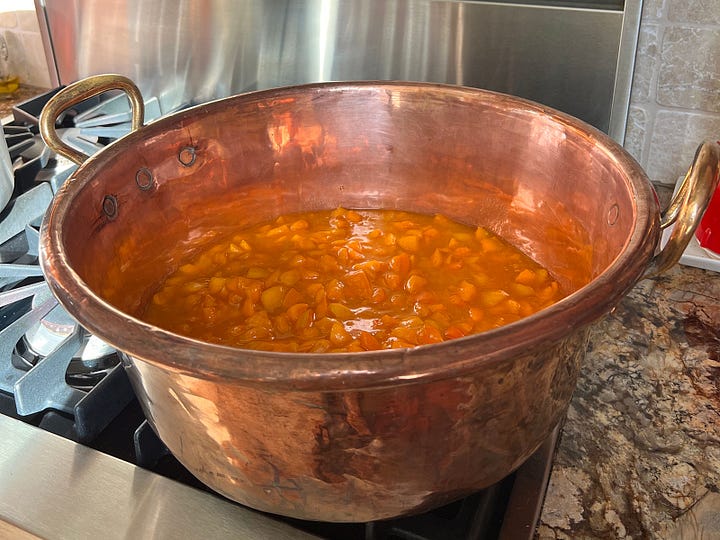 Apricot jam in copper pot and finished apricot jam jars cooling on the counter.