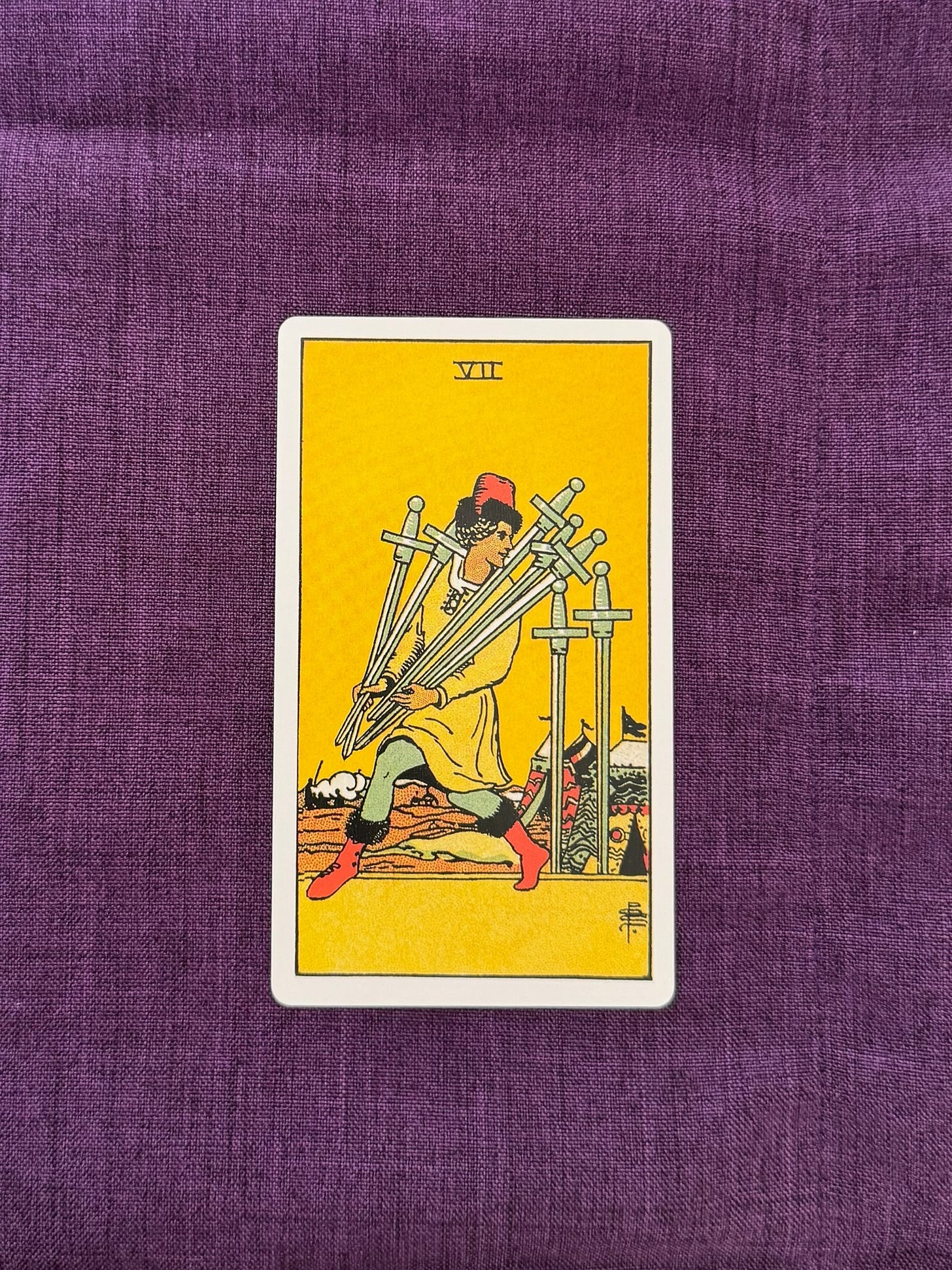 The Seven of tarot card shows the 7 of Swords: a man sneaking away from a military camp with five swords in his arms. He looks over his shoulder at the two upright swords he has left behind. His posture suggests that he is proud of himself for having slipped away without being noticed.