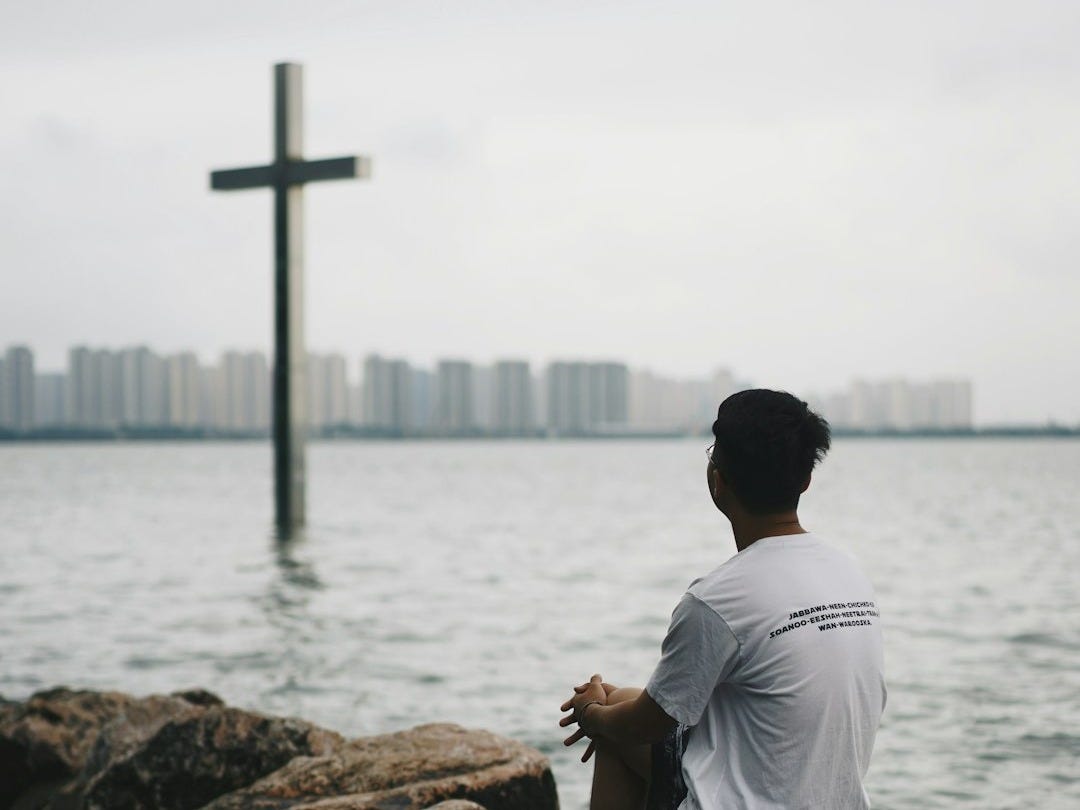 man in white shirt sitting on brown rock near body of water during daytime