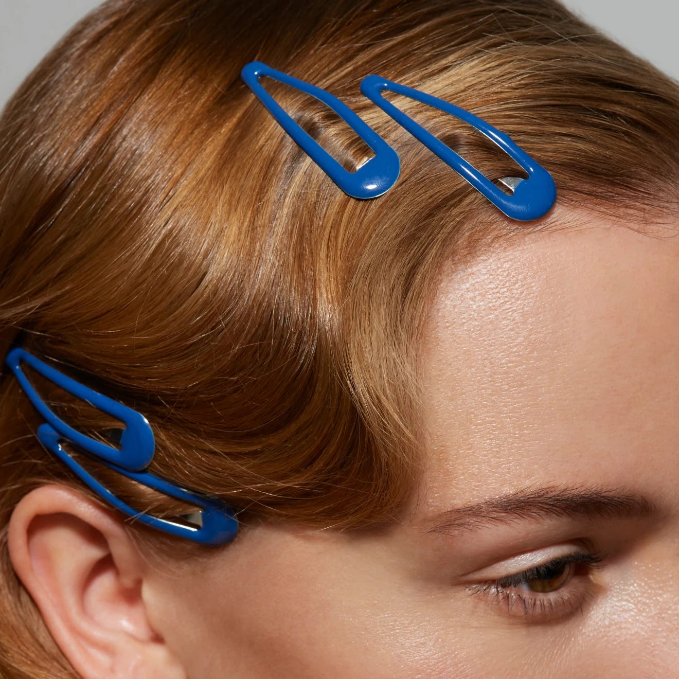 A close-up shot of the top right-hand corner of a white woman’s face, with four bright blue hair slides clipped into her auburn-coloured hair. 