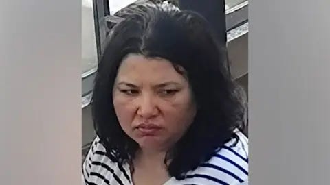 Interpol A woman with dark hair and a serious expression looks down. She wears a striped black and white shirt. Interpol A woman with dark hair and a serious expression looks down. She wears a striped black and white shirt.