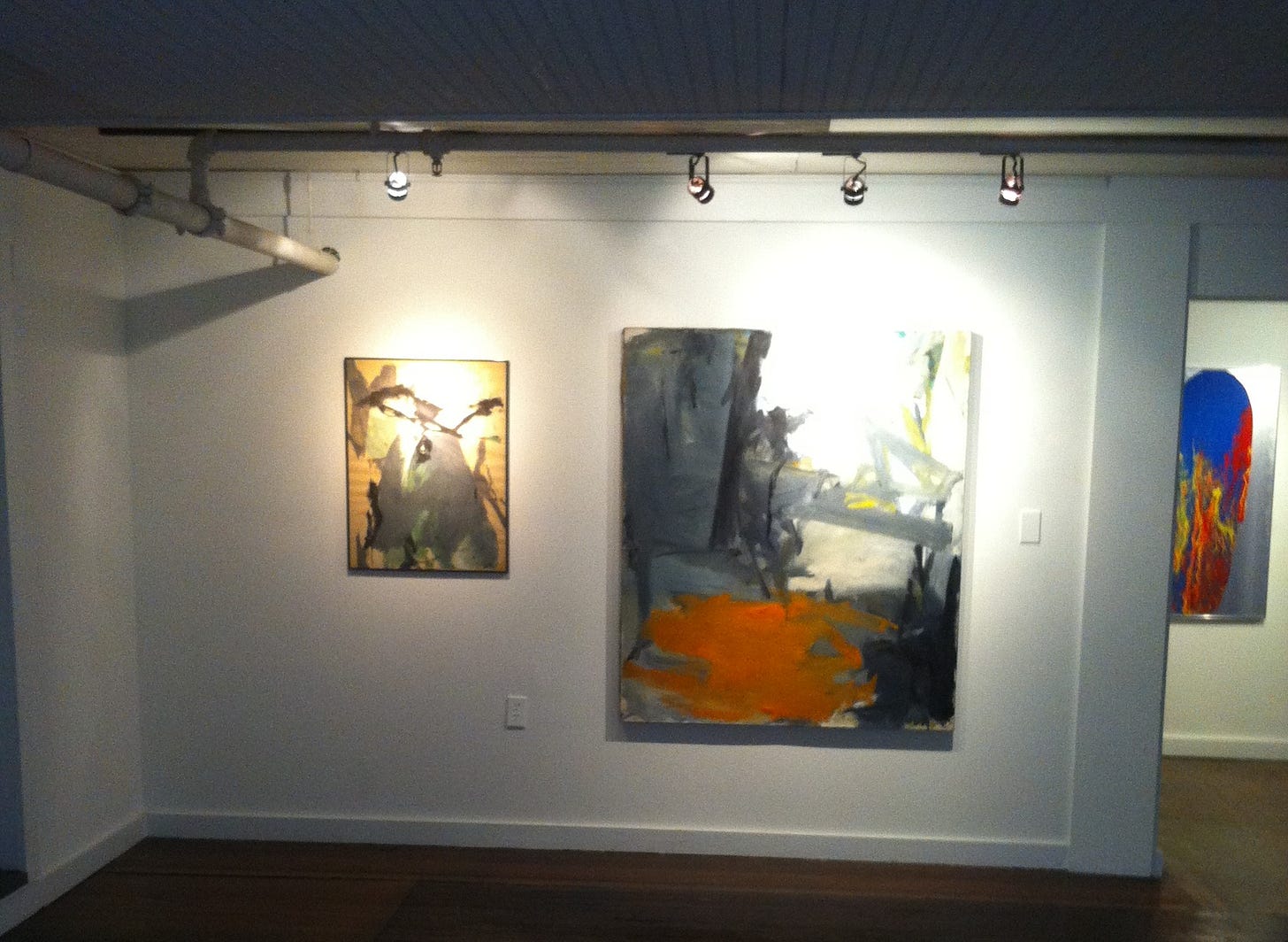 installation view of room full of abstract paintings, highlighting an orange and black abstract facing forward installation view of room full of abstract paintings, highlighting an orange and black abstract facing forward