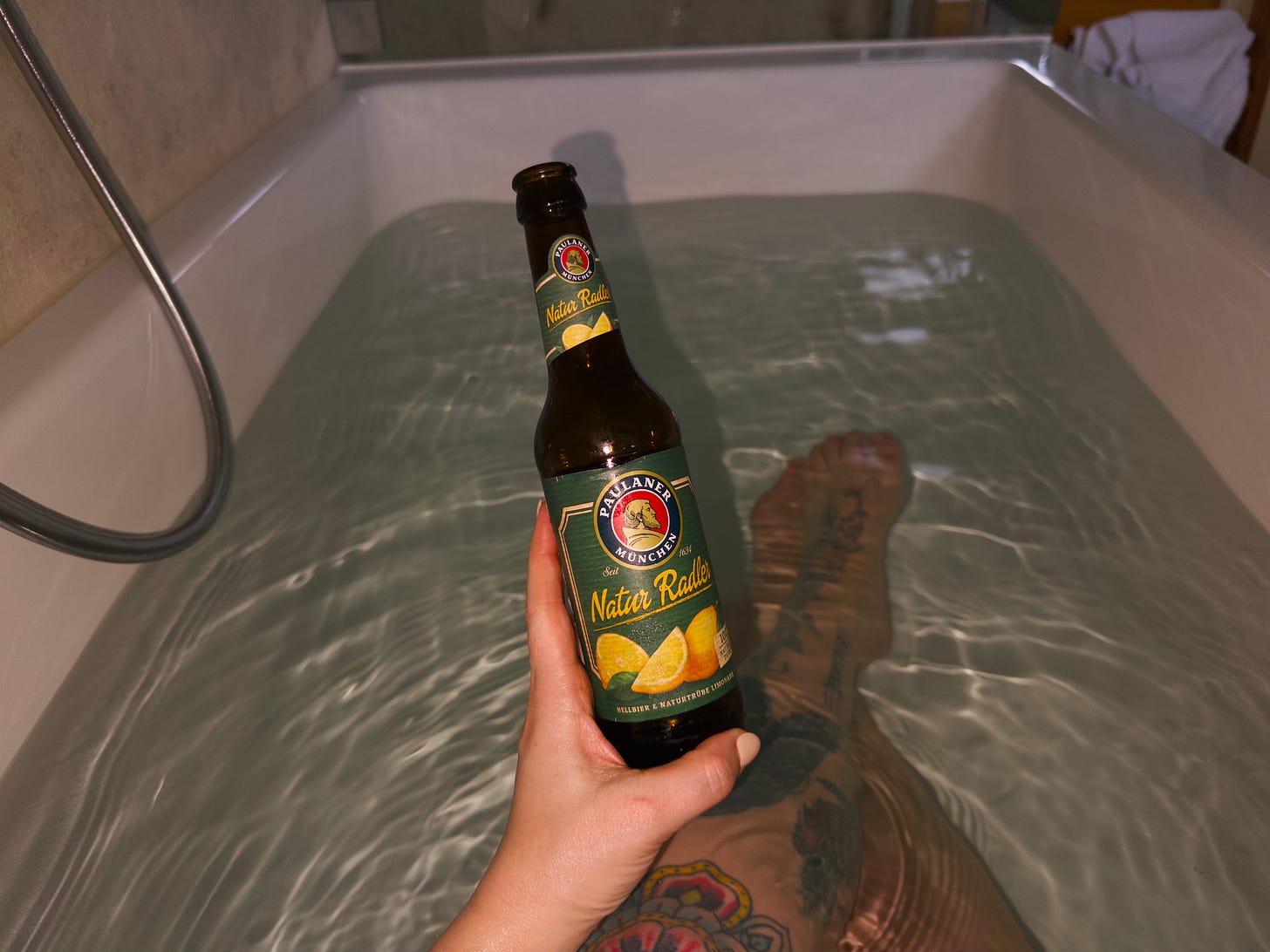 photo of a hand holding a radler, taken in a bathtub