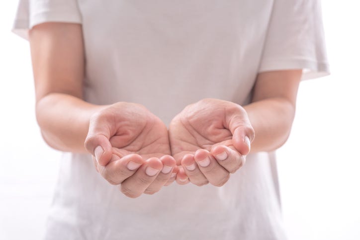 a person in a white t-shirt is holding their hands out toward the camera, palms up, as if they are holding space.