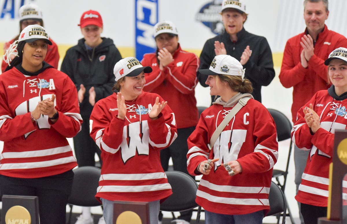 Wisconsin women's hockey players stand behind trophies clapping