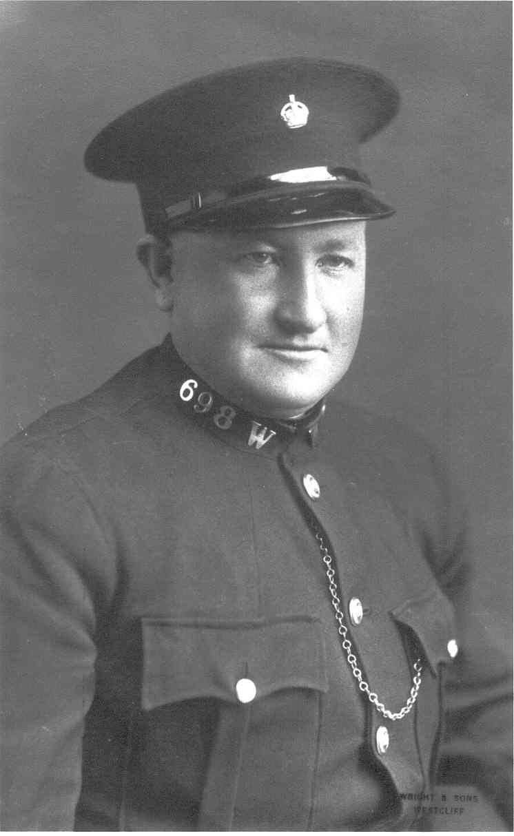 A War Reserve officer in full uniform - the standard police tunic coat with metallic collar number 698W. He also wears the standard police flat cap.