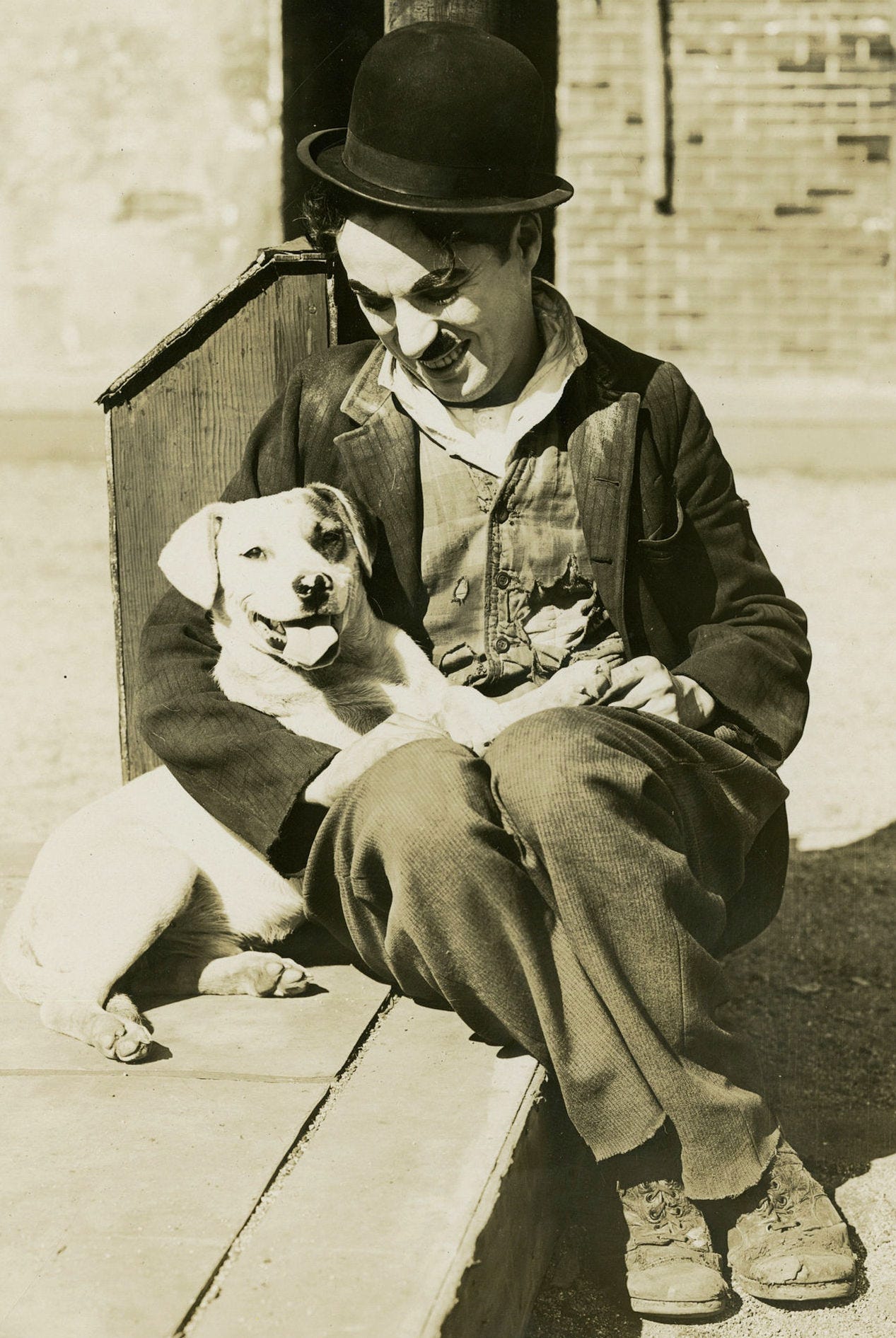 Charlie Chaplin dressed at the Tramp and holding a dog