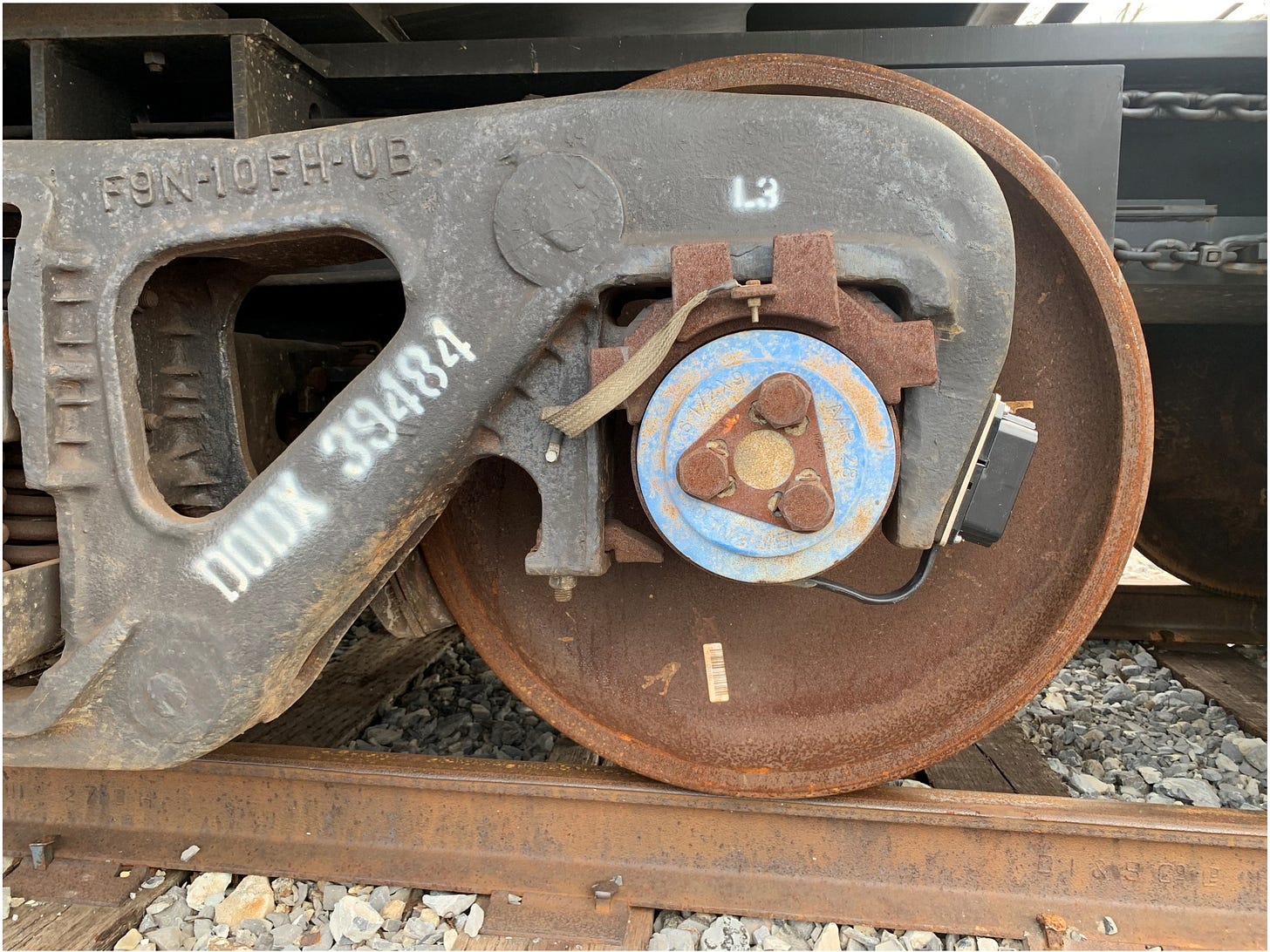 Close-up of a rusty freight train wheel and axle bearing on the track, with stamped car markings. 