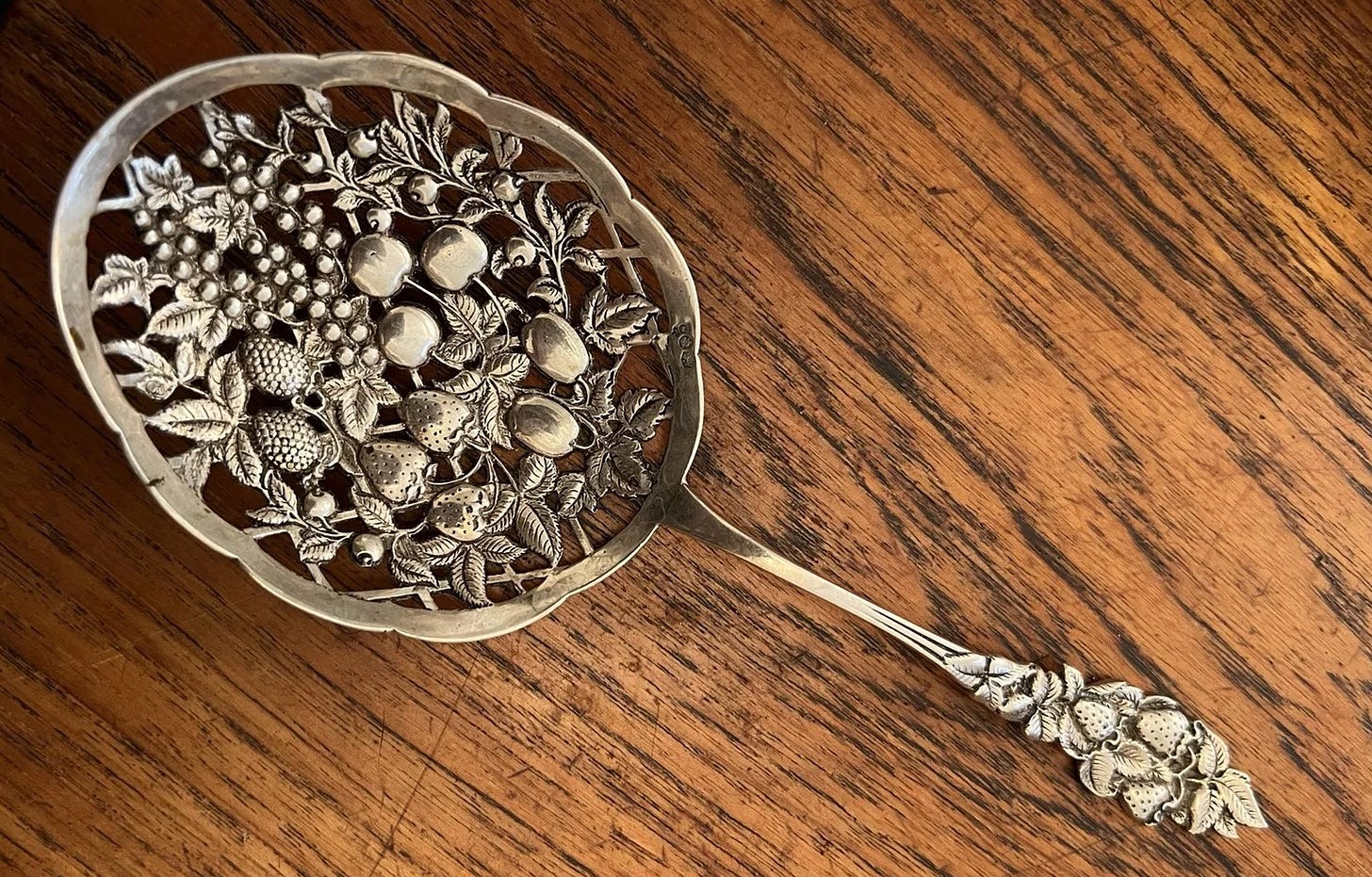 Ornate sterling berry spoon with fruit designs.