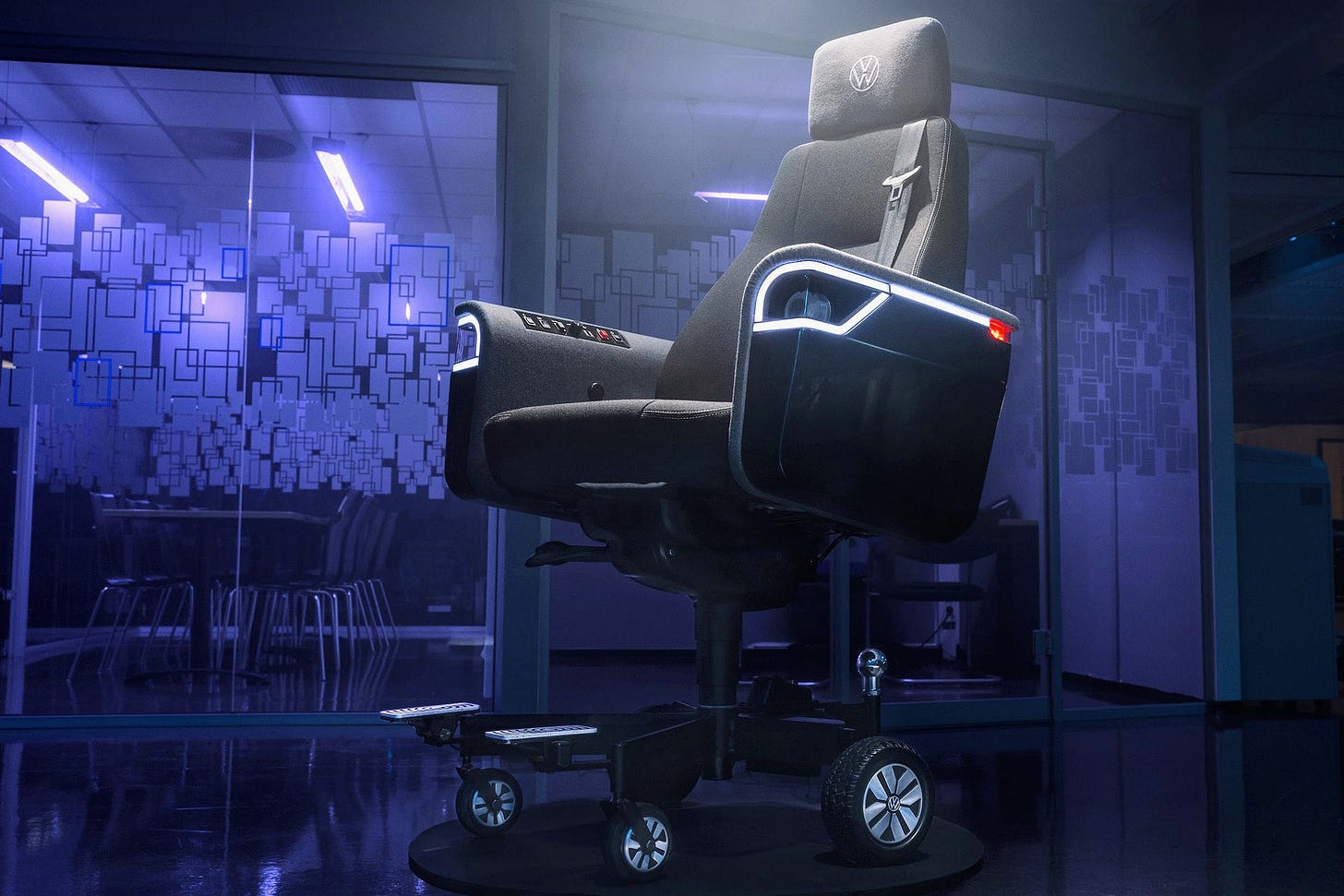 Volkswagen’s chair is ready to party with LED trim around its working headlights, but it’s also ready to drive with a car seatbelt and dedicated metal footrests. The mostly black chair is depicted here in a purple-lit office space with glass doors.