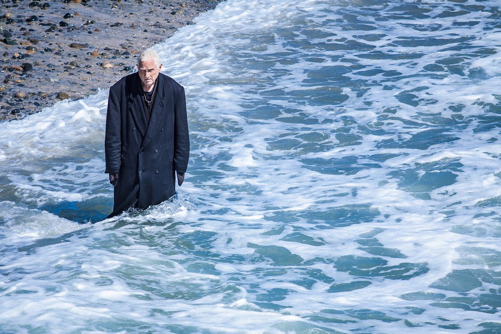 Bruce Parker known as The Trench Coat Guy, wearing his black trench coat as he wades into the surf at Oceanside California