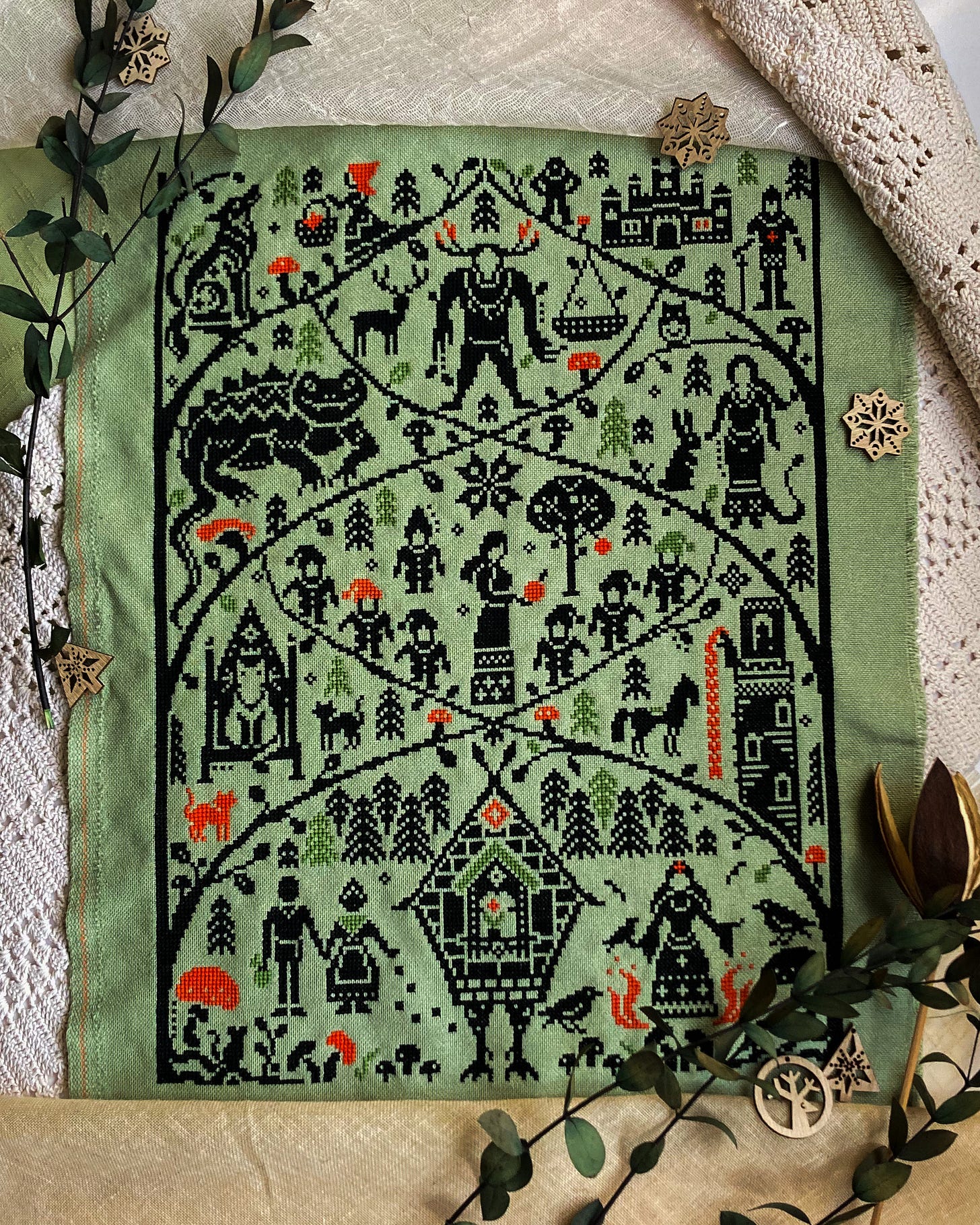 A cross stitch sampler in a monochromatic palette with some pops of red and green show different fairy tales.