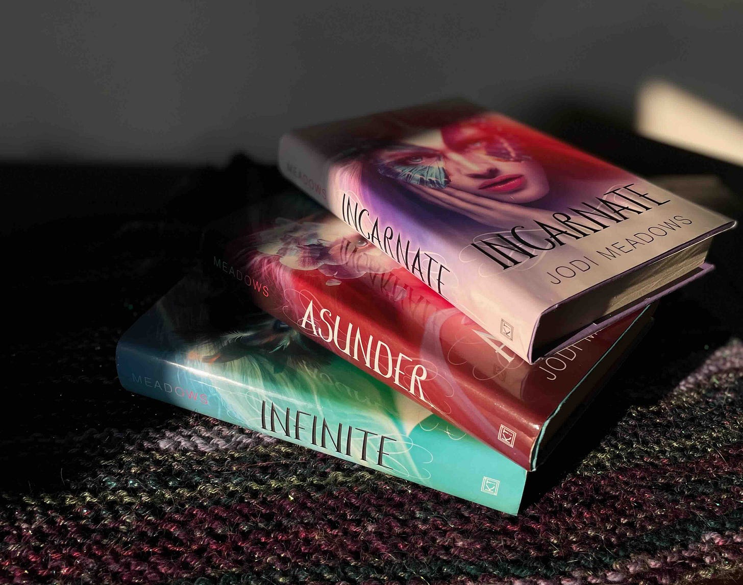 INCARNATE books in both shadow and hard golden-hour light. The first cover features a young woman wearing a butterfly mask. 
