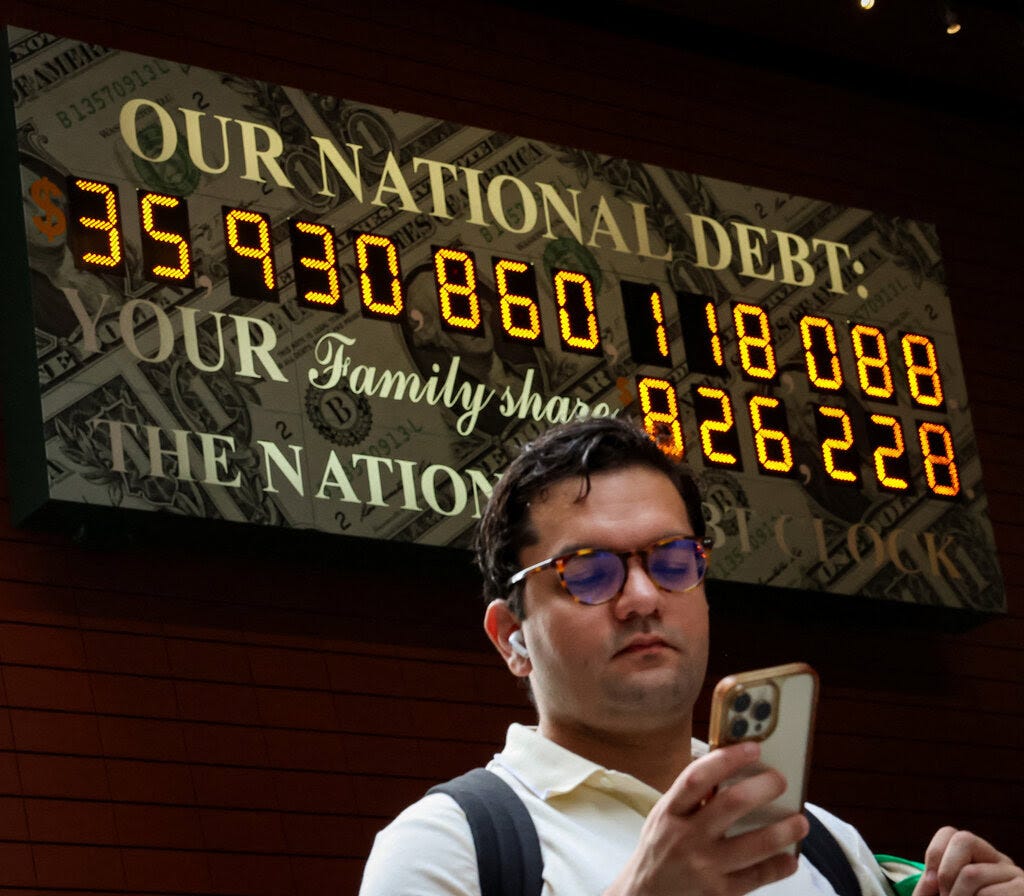 A man looking at his phone in front of the National Debt Clock in New York City.