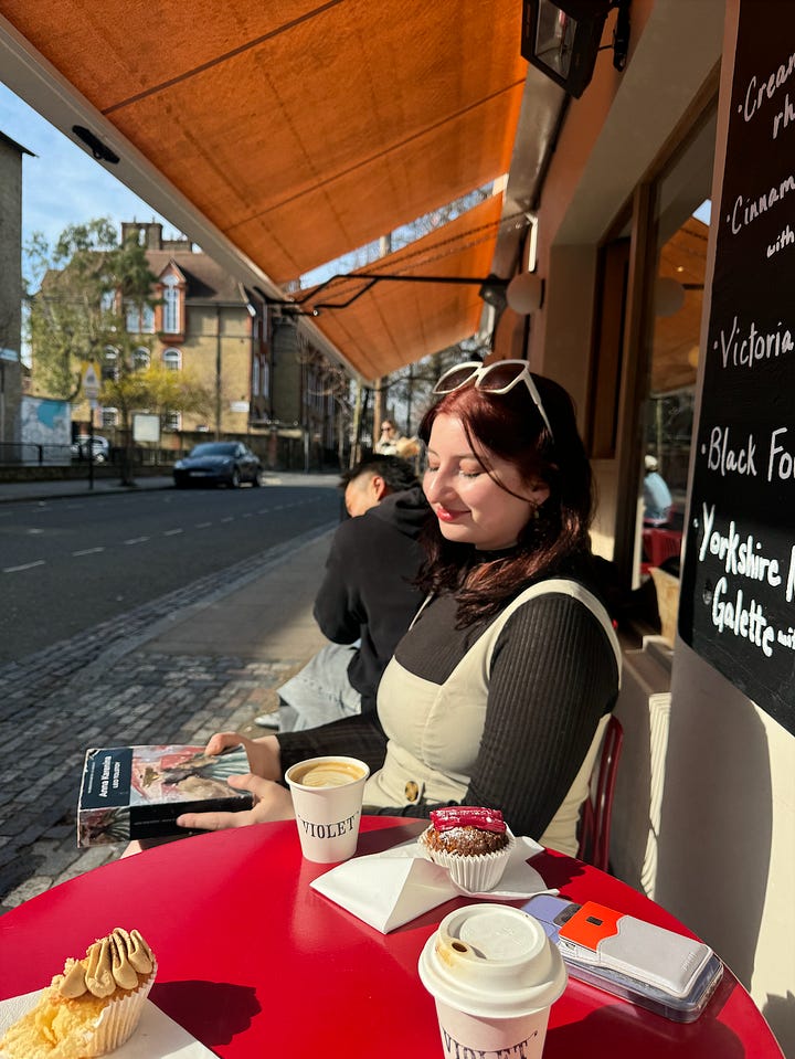 two girls sat outside a café in the sun, one reading 'madonna in a fur coat,' the other holding a copy of anna karenina