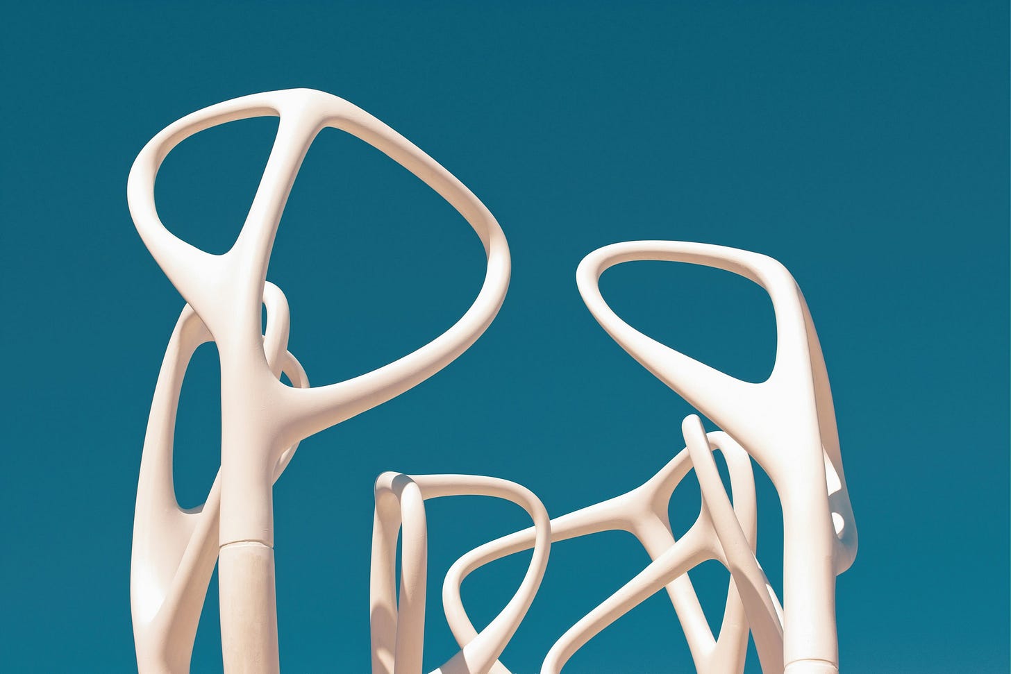 Primo piano di una scultura astratta bianca con forme fluide e organiche simili a ossa o rami intrecciati, stagliata contro un cielo blu limpido e intenso. Primo piano di una scultura astratta bianca con forme fluide e organiche simili a ossa o rami intrecciati, stagliata contro un cielo blu limpido e intenso.