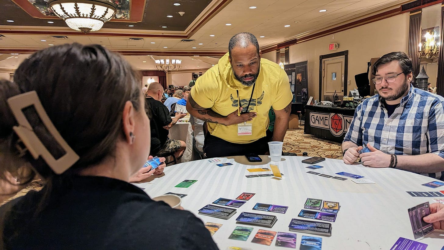three people at a table playing the game with cards in front of them.