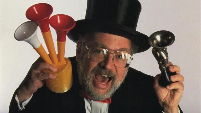 A photo of Dr. Demento wearing a tuxedo and top hat. He has a silly expression and carries several toy horns in his hands.