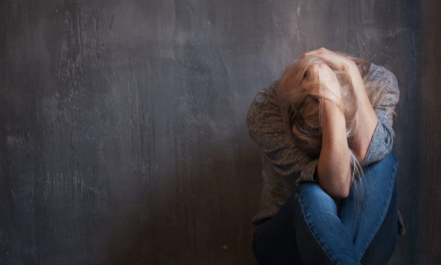 a woman crouching down on the floor, holding her head in her hands, following another incident of intimate partner violence