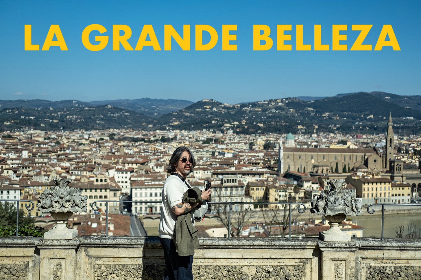 A man with sunglasses standing in front of a view of Florence.