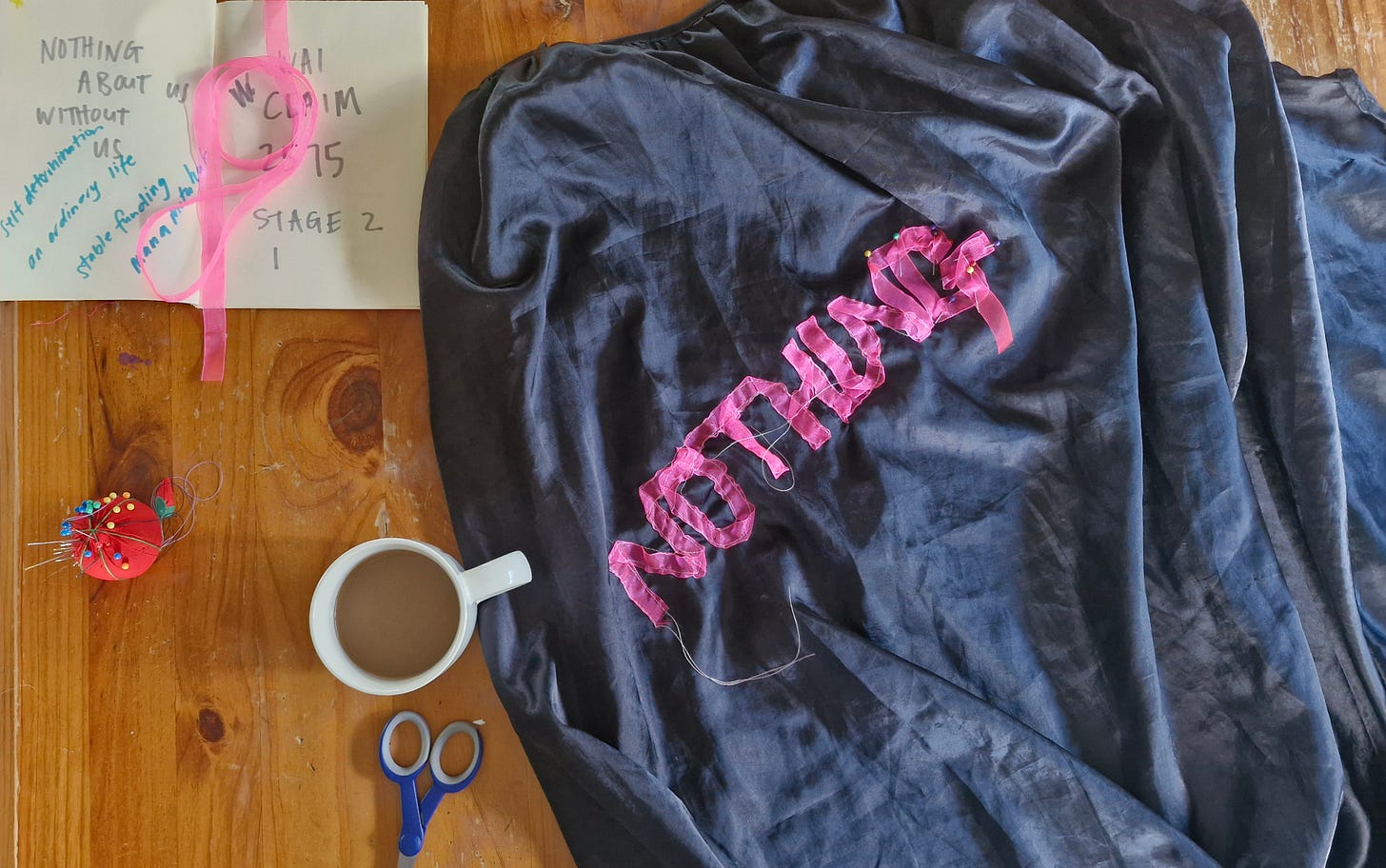flat lay of my notes, pins and ribbon, and the word 'nothing' sewn in pink ribbon on a black cape