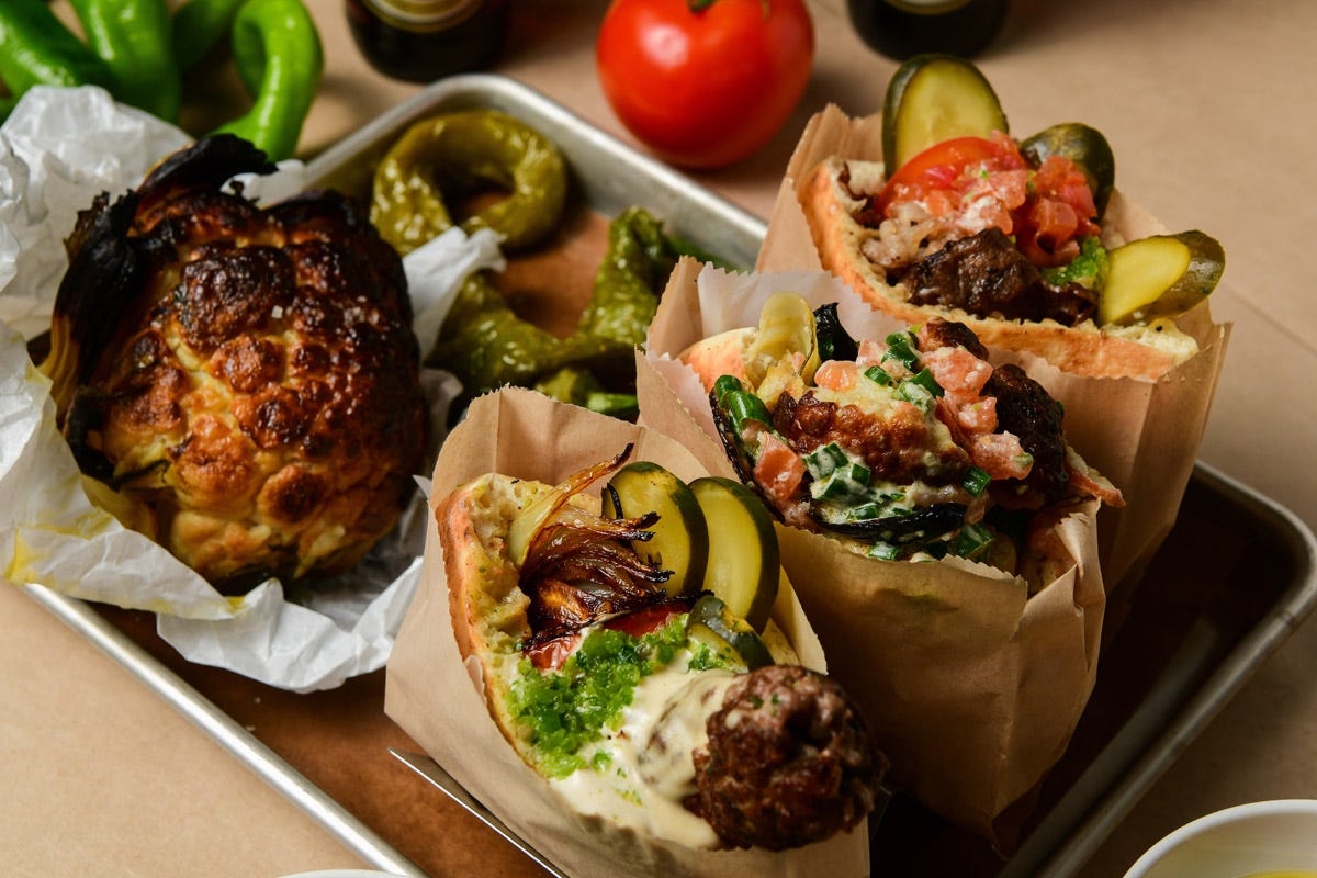 Three stuffed pita breads with meat, pickles, and vegetables, served on a tray with roasted cauliflower and green peppers. Three stuffed pita breads with meat, pickles, and vegetables, served on a tray with roasted cauliflower and green peppers.