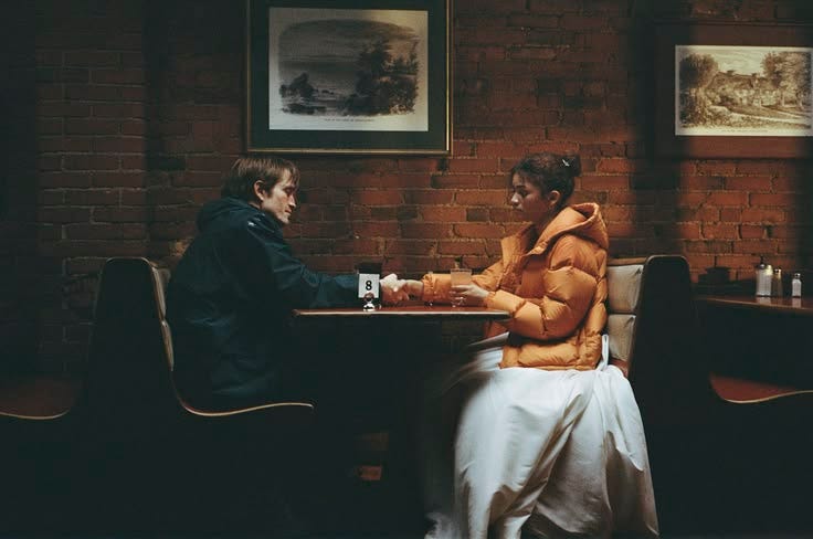 This may contain: two people sitting at a table playing chess in front of a brick wall with pictures on it