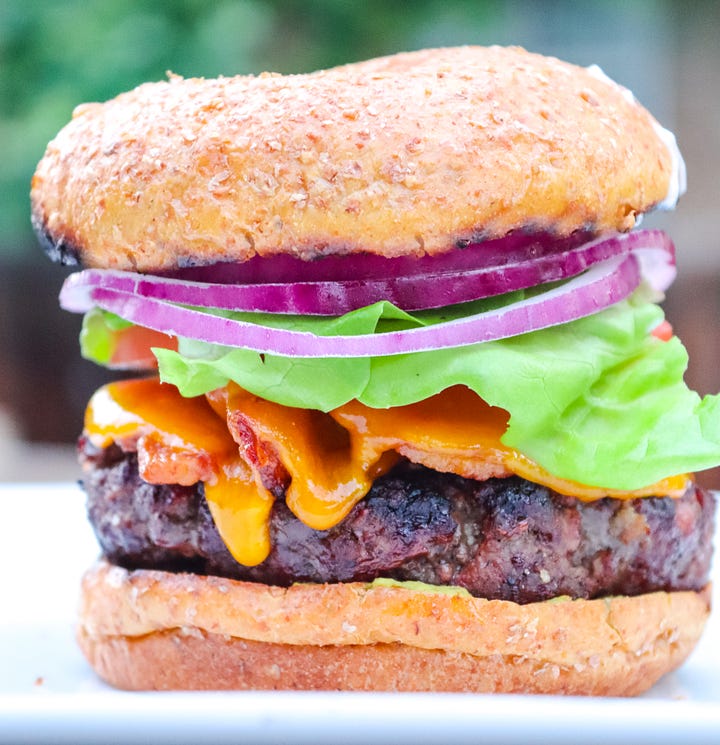 Chef Dave Cook grill hamburgers for Gather Food Studio during an online class. And hamburger with lettuce, onion, tomato and cheese.