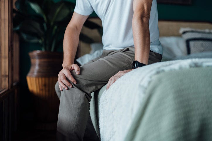 Man holding his knee while sitting on a bed Man holding his knee while sitting on a bed