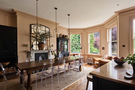 A wooden bay window with blue seat, a soft pink dining room with antique table, a small living room with a sofa and ottoman
