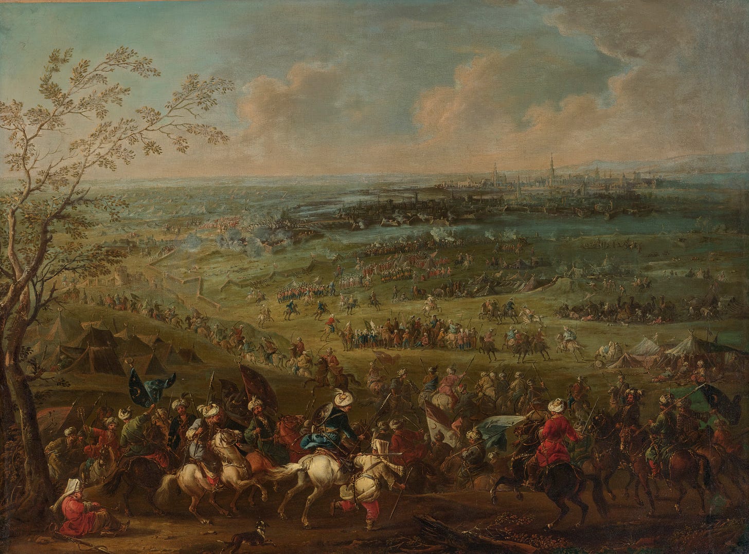 An expansive 18th-century oil painting depicting the Ottoman siege of Vienna. In the foreground, numerous Ottoman soldiers and cavalrymen in colourful robes and turbans gather around horses, tents, flags, and weapons. In the middle distance, lines of soldiers and cavalry move across a large battlefield, with smoke rising from artillery fire. The fortified city of Vienna stretches across the horizon, with church towers and buildings visible beneath a cloudy, muted blue-green sky. A large tree frames the left side of the scene. An expansive 18th-century oil painting depicting the Ottoman siege of Vienna. In the foreground, numerous Ottoman soldiers and cavalrymen in colourful robes and turbans gather around horses, tents, flags, and weapons. In the middle distance, lines of soldiers and cavalry move across a large battlefield, with smoke rising from artillery fire. The fortified city of Vienna stretches across the horizon, with church towers and buildings visible beneath a cloudy, muted blue-green sky. A large tree frames the left side of the scene.