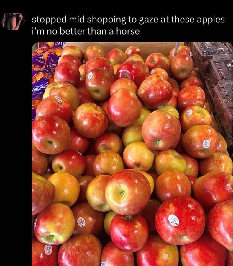 A pile of red and yellow apples displayed in a grocery store. The apples are neatly arranged in a crate, with some bearing small stickers.