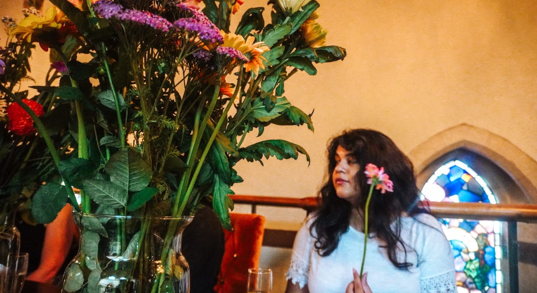 A woman with dark hair holding a flower, with a bouquet of flowers in front of her A woman with dark hair holding a flower, with a bouquet of flowers in front of her