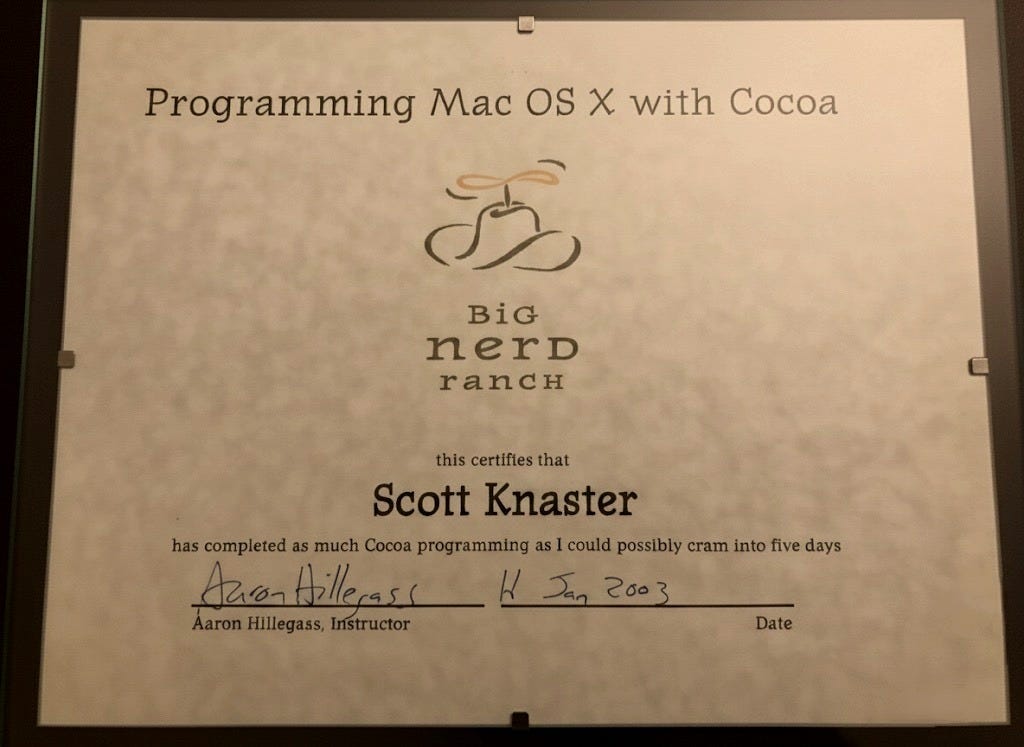 Photo of a certificate that features a drawing of a cowboy hat with a propeller on top (the Big Nerd Ranch logo), with the following text: "Programming Mac OS X with Cocoa / Big Nerd Ranch / This certifies that Scott Knaster has completed as much Cocoa programming as I could possibly cram into five days.  (Signed) Aaron Hillegass, Instructor, 11 Jan 2003, Date"