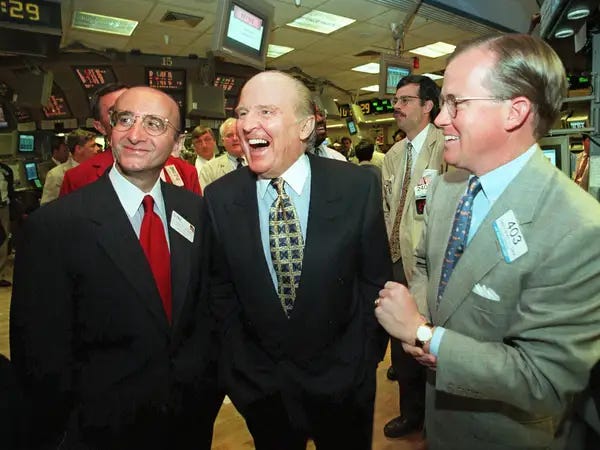 Jack Welch, former CEO of General Electric, laughing on the floor of a stock exchange, flanked by two men in suits.