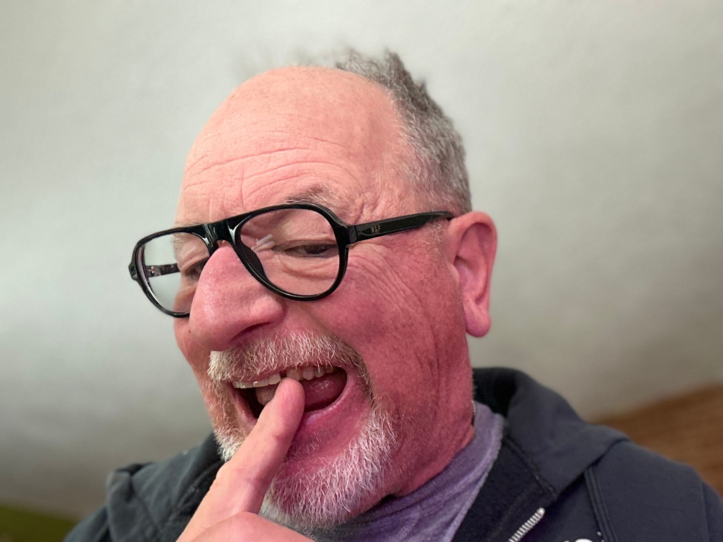 MAN IN HIS SIXTIES POINTING AT A GAP IN HIS TEETH. HE WANTS YOU TO VIEW HIM AS RIDICULOUS, BUT REALIZES THAT HE HAS NO CONTROL OVER  THAT