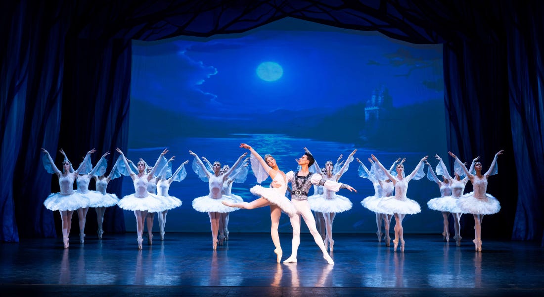 A blue stage with ballet dancers in white tutus, and a male and female posing in the middle A blue stage with ballet dancers in white tutus, and a male and female posing in the middle
