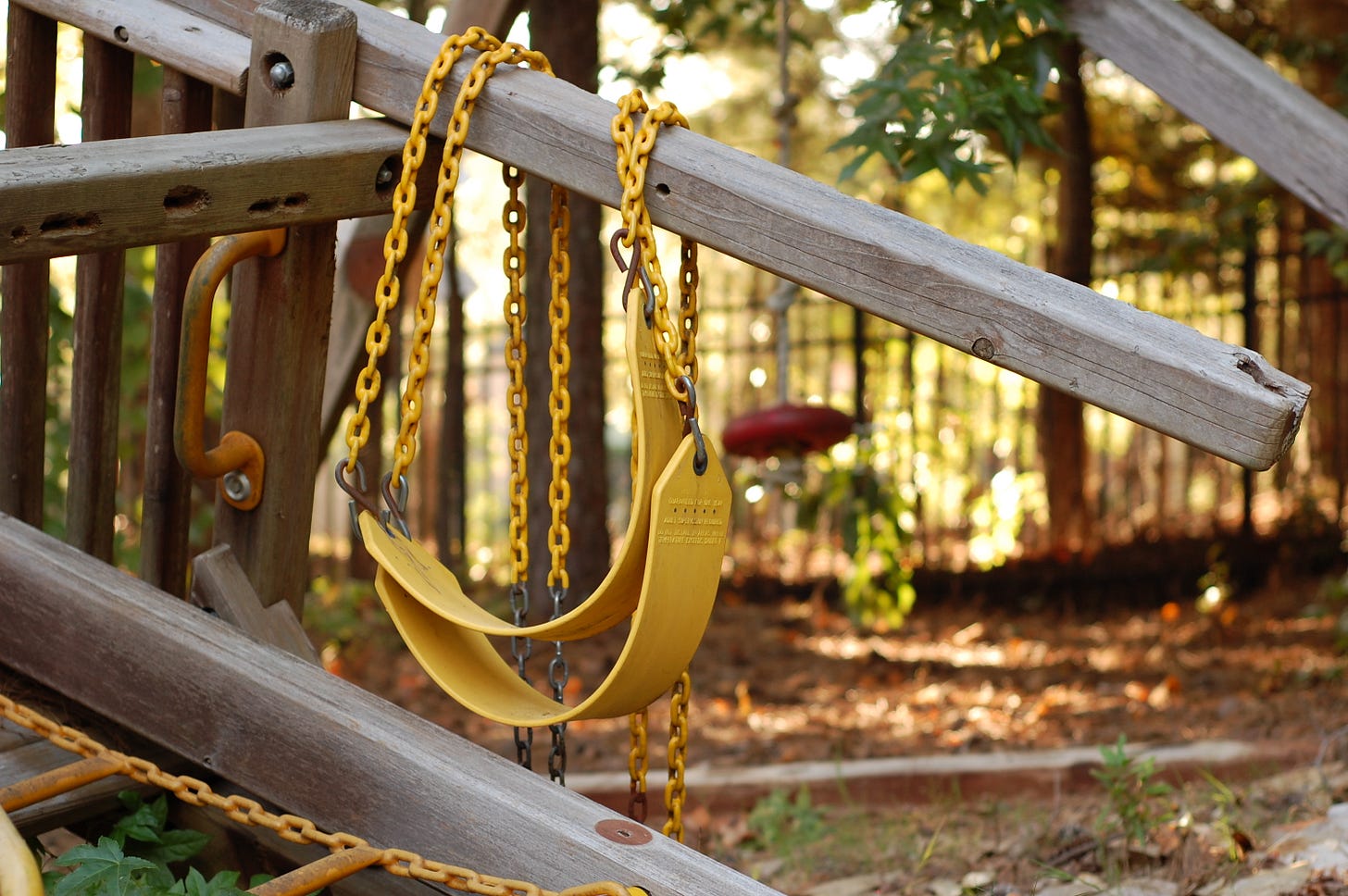 Two yellow swings stacked on the beam of a slumping wooden swingset