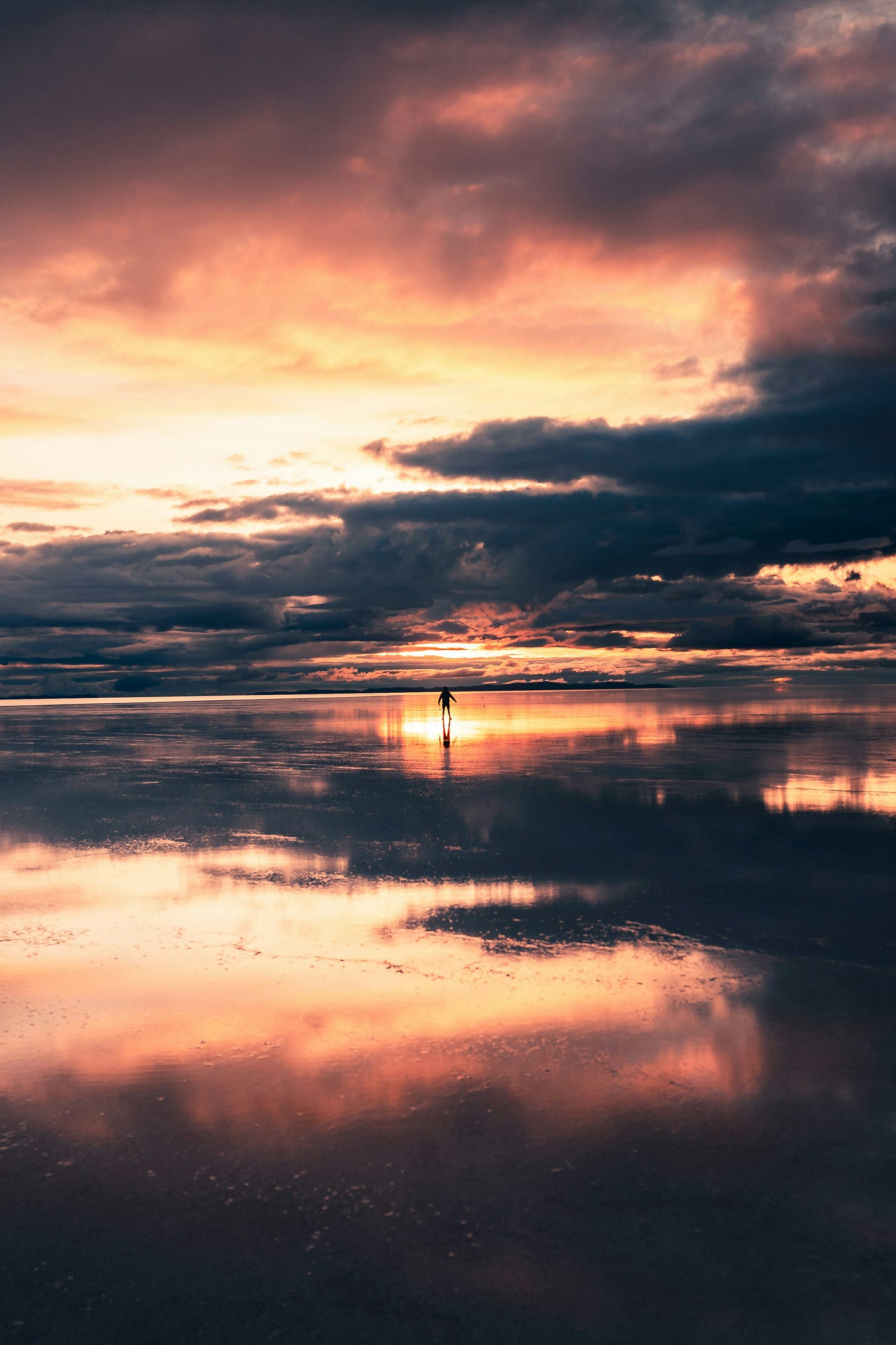 Image of a shore at low tide, during sunset. the red and purple clouds reflected on the wet sand. in the distance a small human figure, walking. Symbolizing human growth and change when coming back through a 'portal'. Image of a shore at low tide, during sunset. the red and purple clouds reflected on the wet sand. in the distance a small human figure, walking. Symbolizing human growth and change when coming back through a 'portal'.