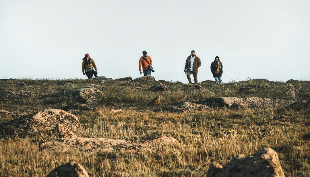 a group of people walking across a grass covered field a group of people walking across a grass covered field