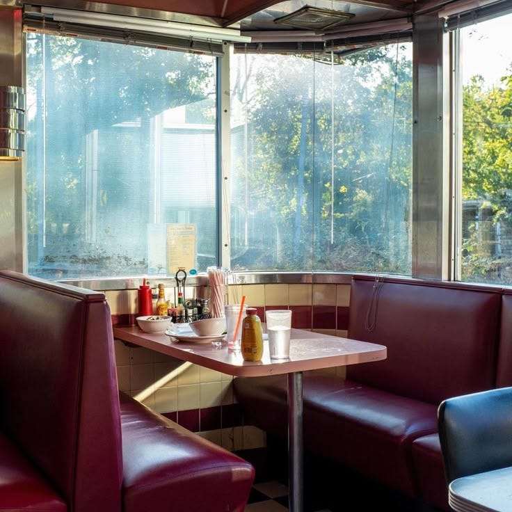 This may contain: two booths in a restaurant with red leather seats and tables next to each other near large windows