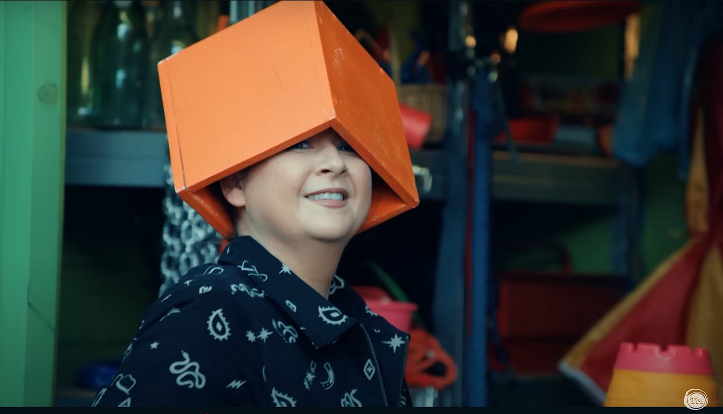 Rosie Ramsey smiles at the camera with an orange box on her head.