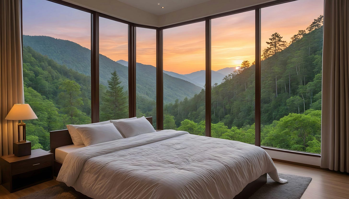Bed in hotel room overlooking mountains and sunset