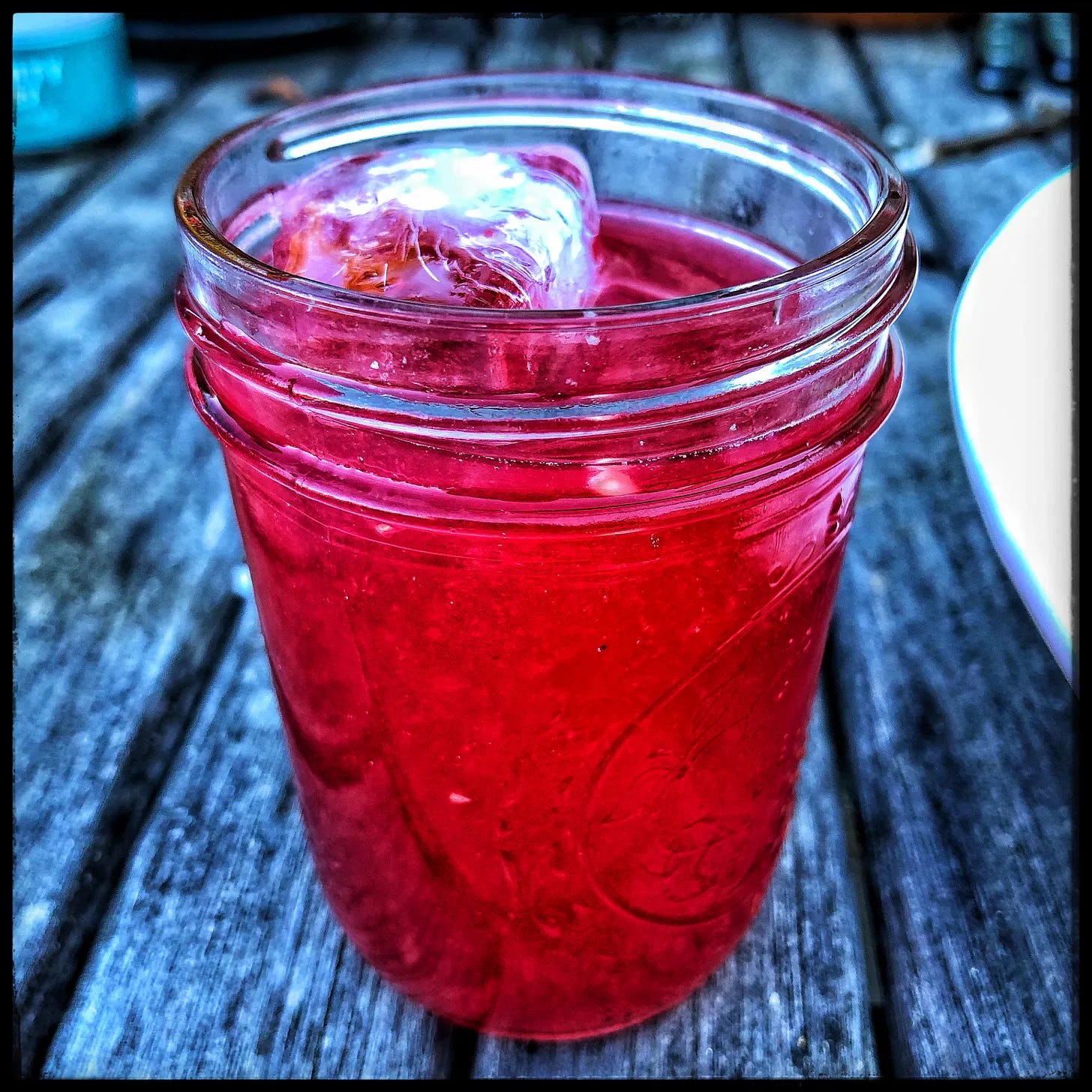 Mason jar filled with smashed cherries, gin, and ice resting on a weathered wooden table. Mason jar filled with smashed cherries, gin, and ice resting on a weathered wooden table.