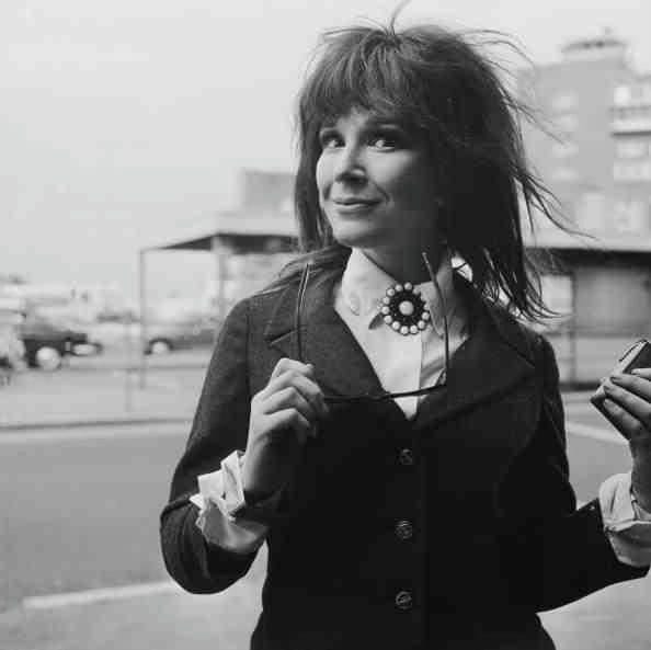 Fenella Fielding at London Airport 1968 wearing 1960s suit, with brooch, with long hair and glasses .